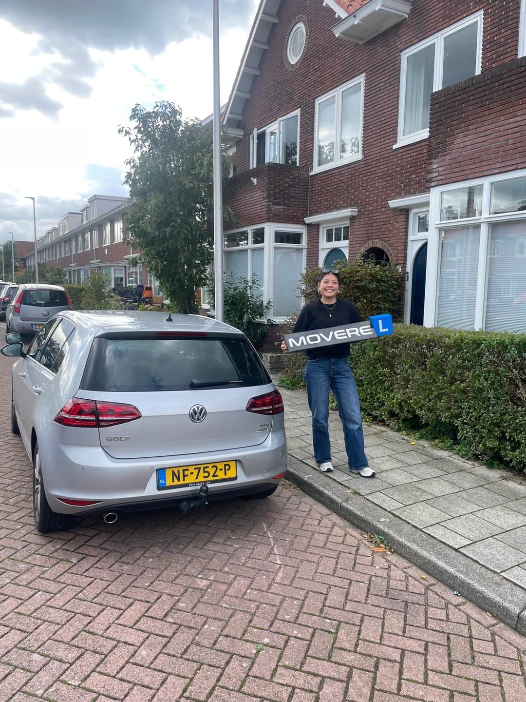 Geslaagde leerling met Movere rijschool bord naast de VW Golf
